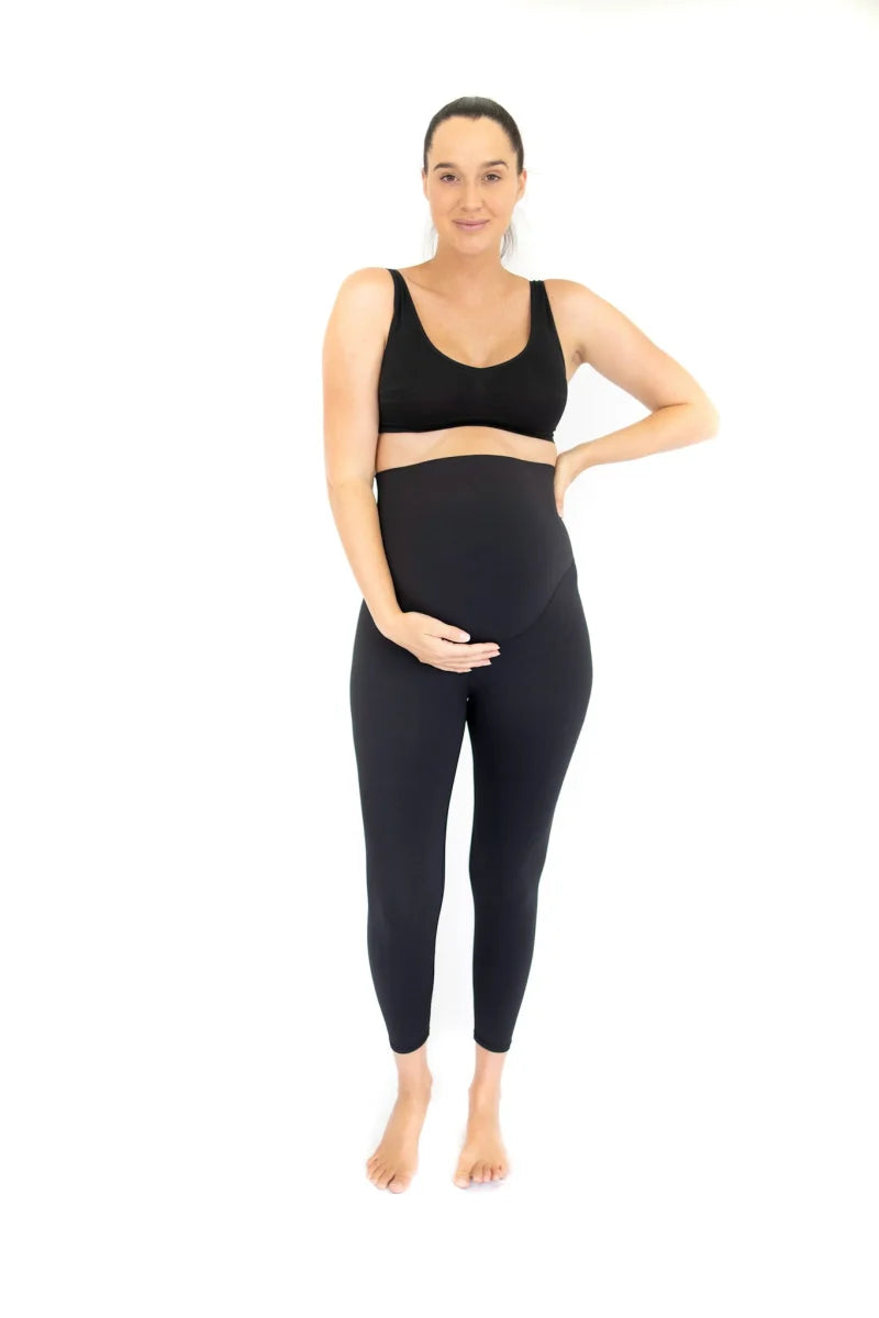 Pregnant woman in black Emamaco maternity leggings standing confidently with hand on hip