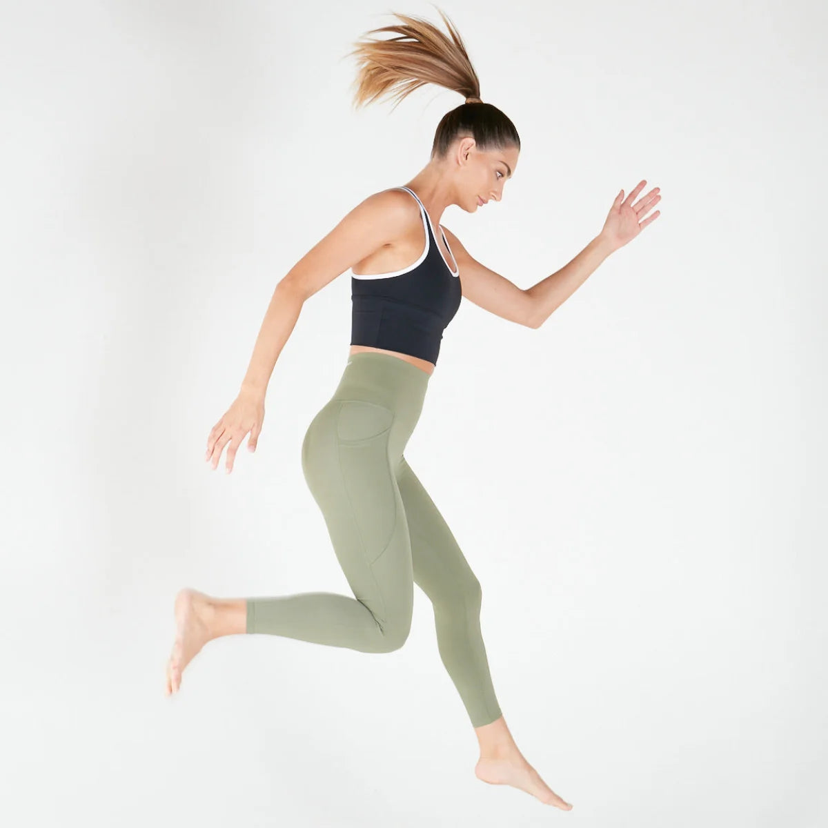 Woman in athletic wear mid-air wearing 7/8 Shaper Move Leggings in Olive on final sale