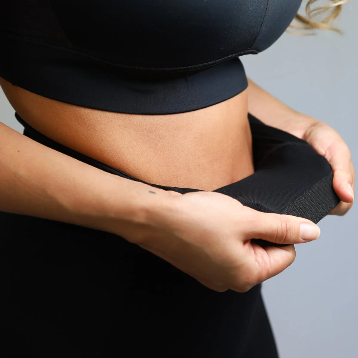 Hands adjusting a midriff-baring black athletic outfit from Introducing Emamaco Shapewear