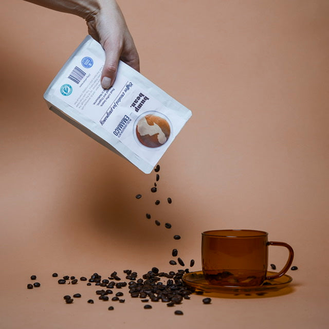 Coffee beans pouring from a package into a cup of Bump Bean coffee for breastfeeding mums