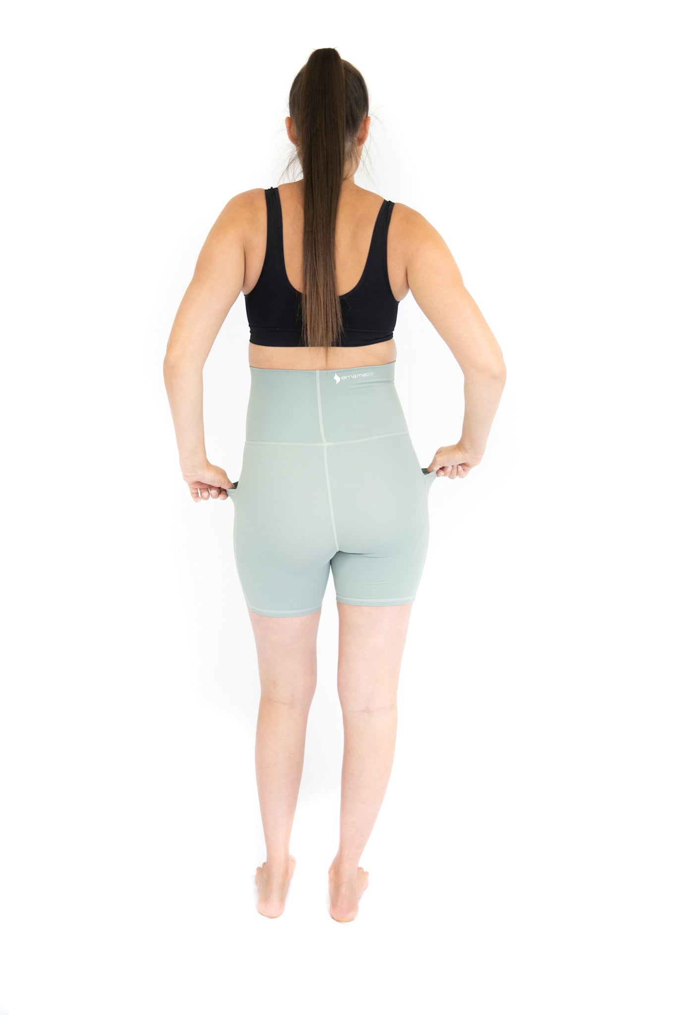 Woman in black sports bra and blue high-waisted shorts showcasing EmamaCo maternity shorts