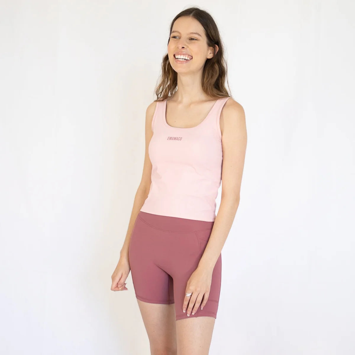 Smiling woman in pink tank top and mauve shorts, perfect for Emamaco Everyday at the yoga studio