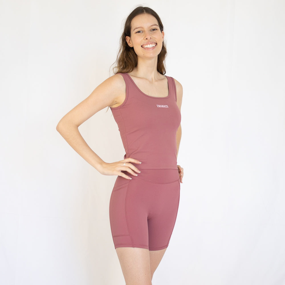 Woman in pink Emamaco Everyday Singlet at yoga studio, showcasing fitted workout shorts